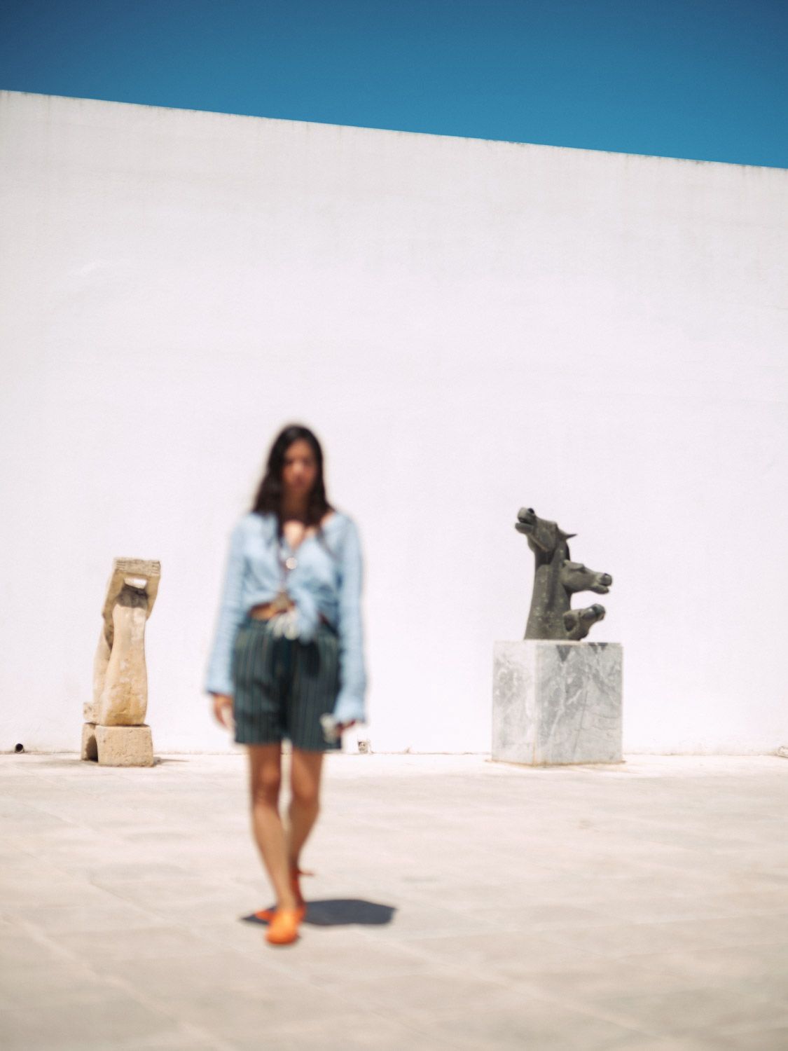 An image of Tania Feghali, blurry, between two stone statues at Vorres Museum in Greece